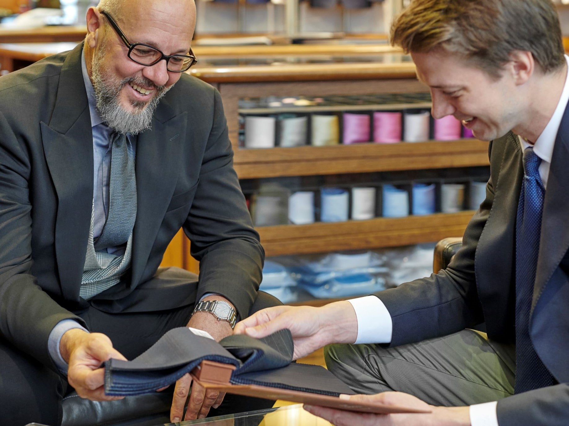 Two men in a store, one showing fabric to the other