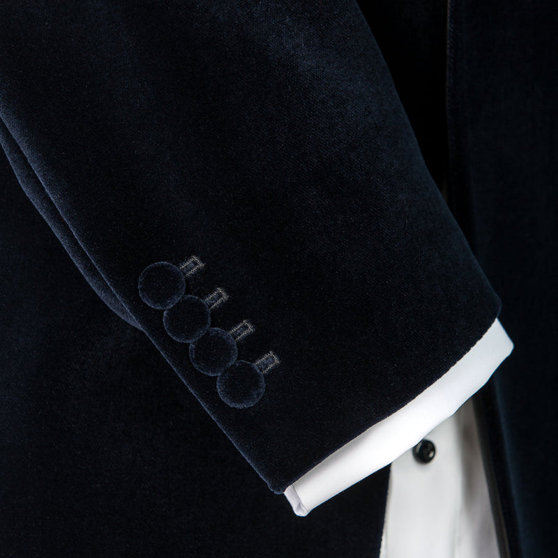 Close-up of a dark blue velvet jacket cuff with white shirt collar on a black background