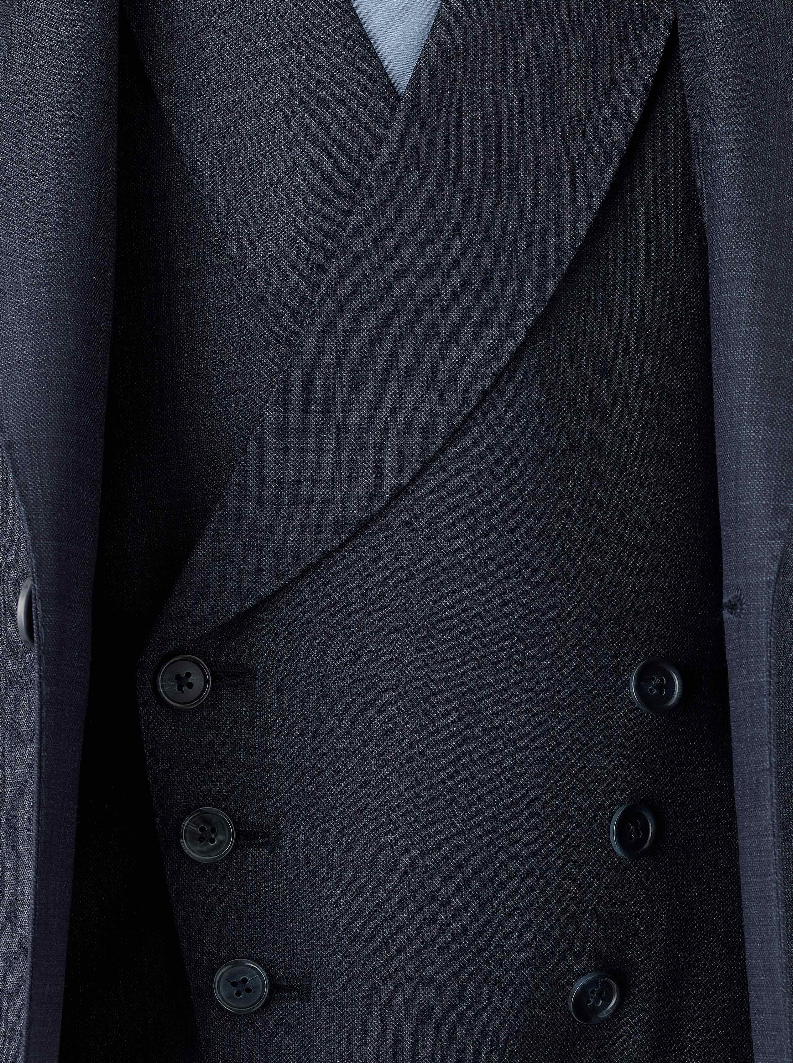 A double-breasted blue waistcoat crafted from Super 130s Italian wool, featuring a 3x3 button design with grey horn buttons, welt pockets, and a straight bottom. The navy lining matches the jacket, while the back lining includes a belt and buckle for an adjustable fit.