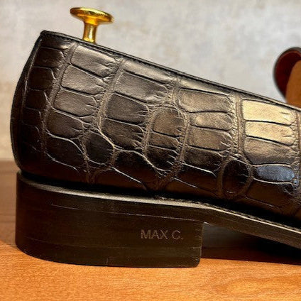 Black leather shoe with crocodile pattern on a wooden surface