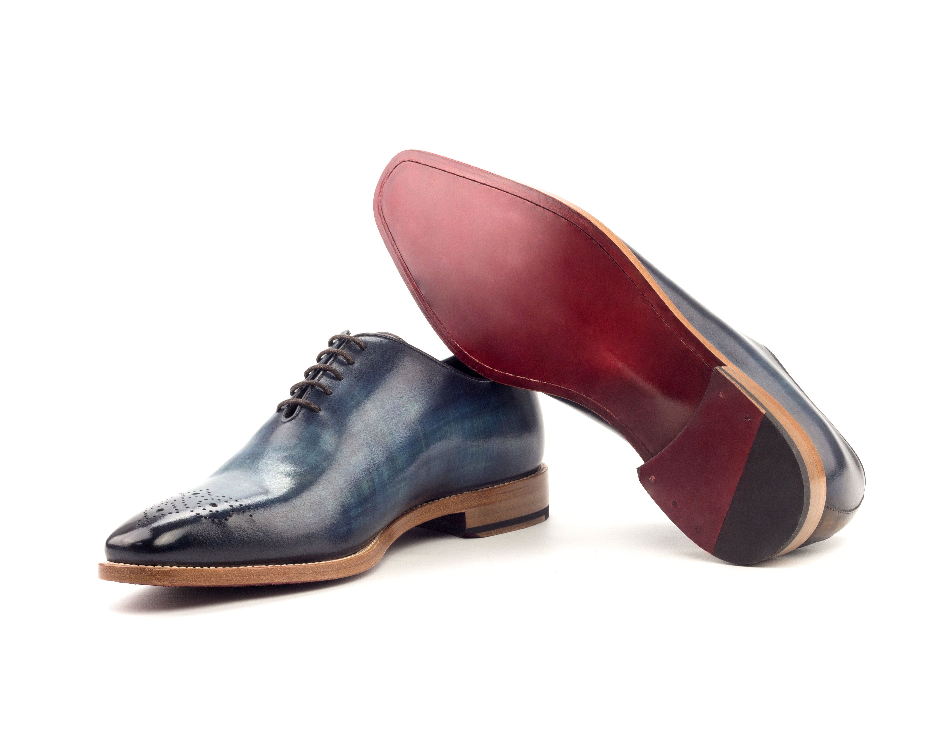 Pair of blue dress shoes with red sole on a white background