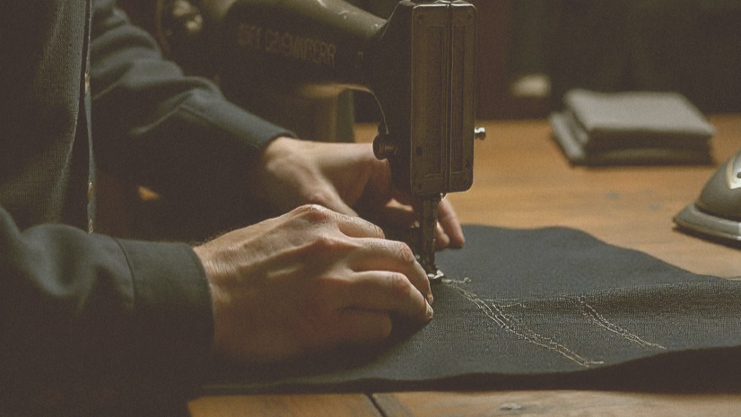 Person working on a sewing machine with suits in the background