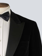 A black velvet dinner jacket designed for black-tie events, featuring a single-breasted one-button closure with a link button, silk peak lapels, and elegant paisley lining. Details include silk-covered buttons, double vents, a handkerchief pocket, and slanted silk pocket flaps that can be tucked in for a jetted look.
