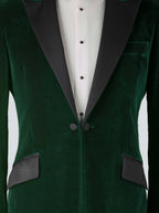 A green velvet dinner jacket designed for black-tie events, featuring a single-breasted one-button closure with a link button, silk peak lapels, and elegant paisley lining. Styled with a classic white dinner shirt with a Marcella front and dress studs, adding timeless sophistication to the ensemble.