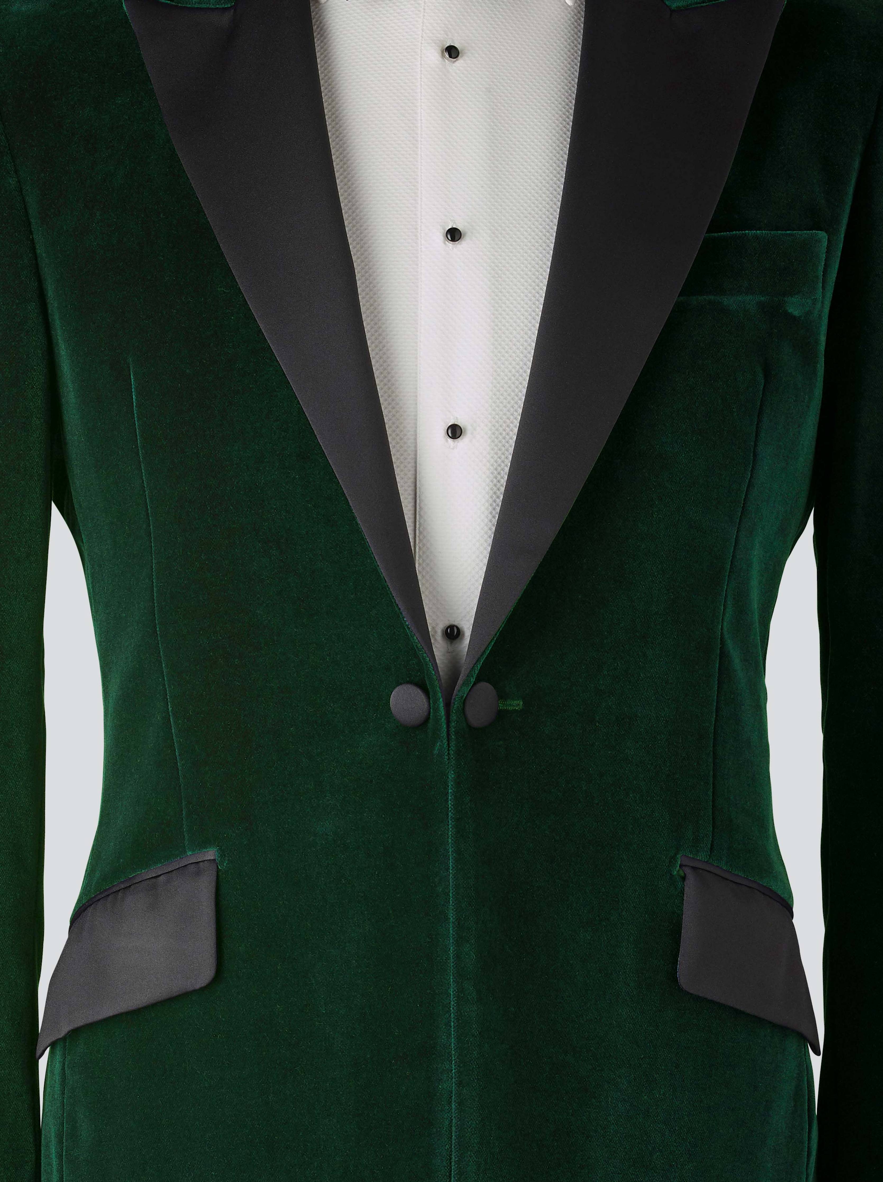 A green velvet dinner jacket designed for black-tie events, featuring a single-breasted one-button closure with a link button, silk peak lapels, and elegant paisley lining. Styled with a classic white dinner shirt with a Marcella front and dress studs, adding timeless sophistication to the ensemble.