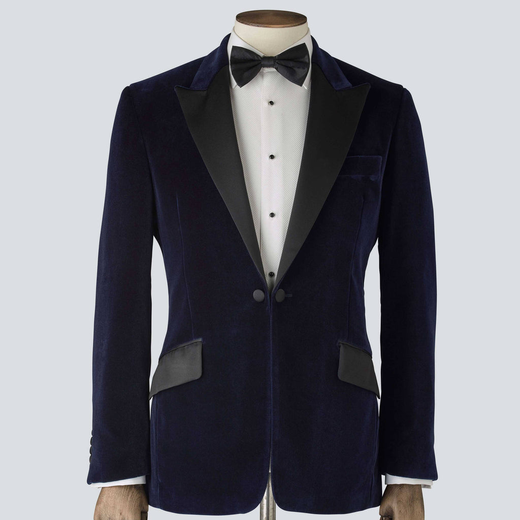 A navy blue velvet tailored dinner jacket with a classic collar, silk peak lapels, and a single-breasted design. 