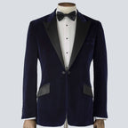 A navy blue velvet tailored dinner jacket with a classic collar, silk peak lapels, and a single-breasted design. 